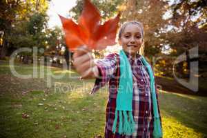 Portrait of smiling girl showing autumn leaf at park