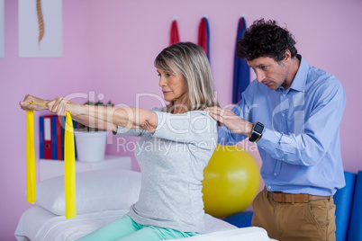 Senior woman training with exercise band assisted by physiothera