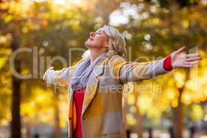 Woman standing with arms outstretched against autumn trees