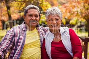 An elderly couple smiling at the camera sitting on the bench