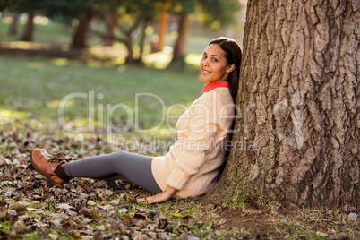 Portrait of woman sitting by tree at park