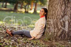Portrait of woman sitting by tree at park