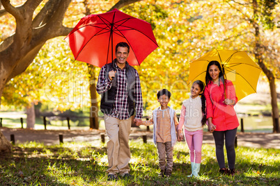 Happy family walking with umbrellas at park