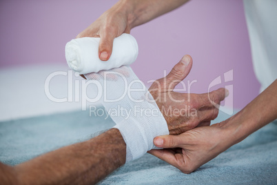 Physiotherapist putting bandage on injured hand of patient