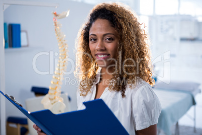 Smiling physiotherapist holding clipboard in clinic