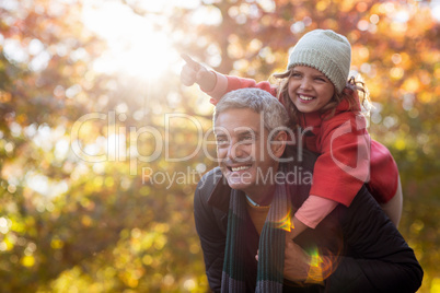 Father piggybacking daughter against autumn trees