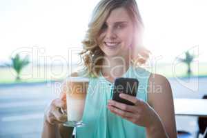 Smiling woman holding a coffee glass and using her mobile phone