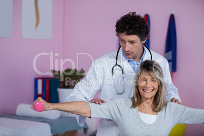 Physiotherapist assisting senior woman to lift dumbbellÂ&#x