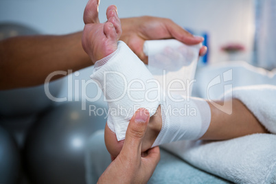 Physiotherapist putting bandage on injured feet of patient