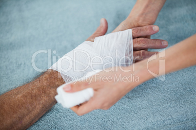 Physiotherapist putting bandage on injured hand of patient