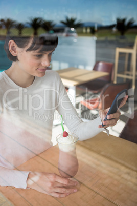 Woman using mobile phone while having milkshake