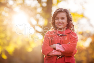 Cute girl with arms crossed against autumn tree