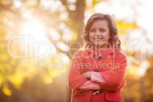 Cute girl with arms crossed against autumn tree