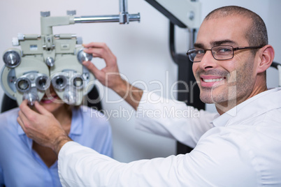 Smiling optometrist examining female patient on phoropter