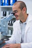 Smiling male optometrist looking through microscope