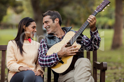 Smiling man with woman playing guitar on bench