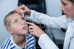 Female optometrist putting eye drop in young patient eyes