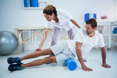 Physiotherapist doing leg therapy to a man using foam roll