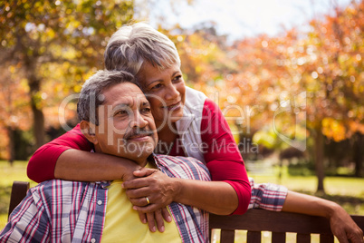 An elderly woman hugs her husband sitting on the bench