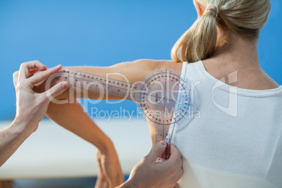 Male therapist measuring female patient shoulder with goniometer