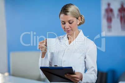 Physiotherapist looking at medical report while having coffee