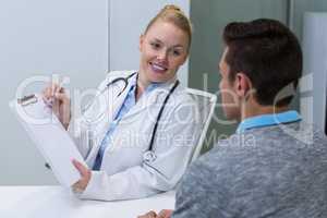 Smiling female doctor explaining patient on clipboard