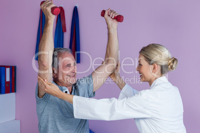 Physiotherapist assisting senior man to lift dumbbellÂ&#xa0