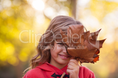 Girl covering face with autumn leaves