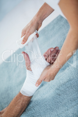 Physiotherapist putting bandage on injured hand of patient