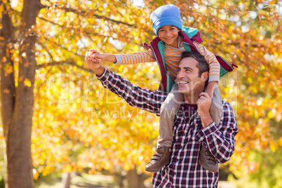 Father carrying son on shoulder against autumn tree