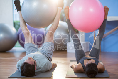 Man and woman holding exercise ball between legs