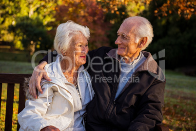Elderly couple sitting on bench smiling at each other in park