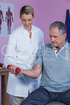Physiotherapist assisting senior man to lift dumbbellÂ&#xa0