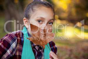 Portrait of girl hiding mouth with autumn leaf