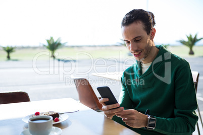 Man using mobile phone with cake and cup of coffee on table
