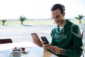 Man using mobile phone with cake and cup of coffee on table