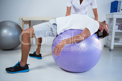 Physiotherapist assisting man with exercise ball