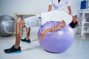 Physiotherapist assisting man with exercise ball
