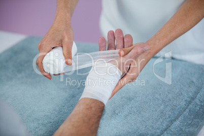 Physiotherapist putting bandage on injured hand of patient