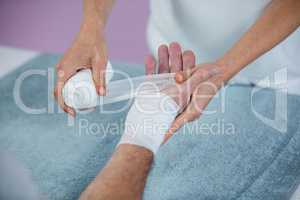 Physiotherapist putting bandage on injured hand of patient