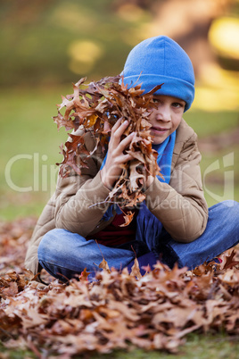 Portrait of boy holding autumn leaves at park