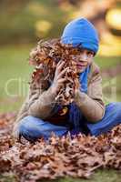 Portrait of boy holding autumn leaves at park