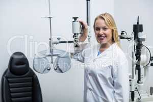 Smiling female optometrist standing near phoropter