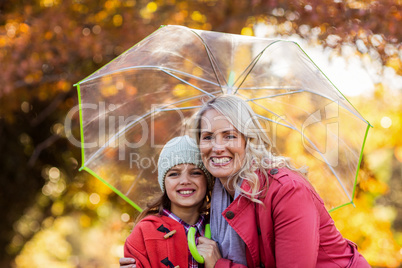 Mother and daughter embracing while holding umbrella