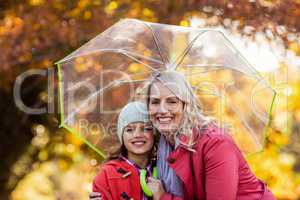 Mother and daughter embracing while holding umbrella