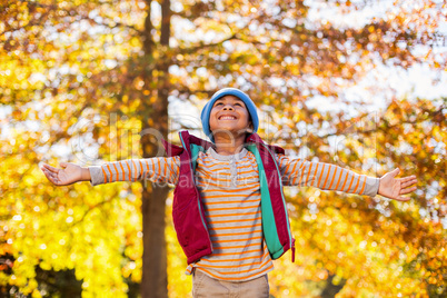 Happy boy with arms outstretched against autumn trees
