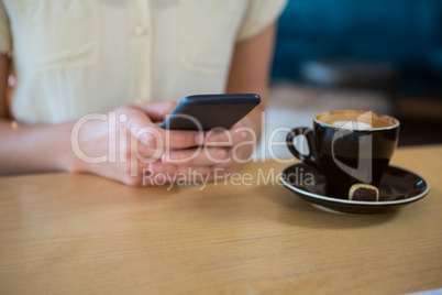 Woman using mobile phone with coffee cup on table