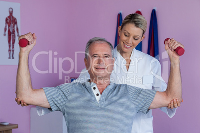 Physiotherapist assisting senior man to lift dumbbellÂ&#xa0