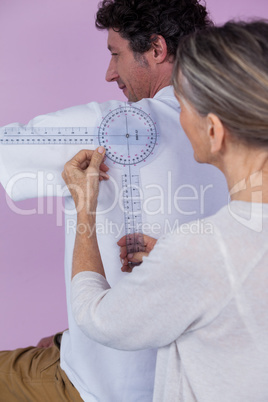 Physiotherapist measuring male patients back with medical ruler