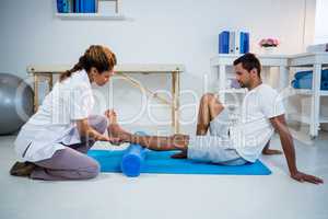 Physiotherapist doing leg therapy to a man using foam roll